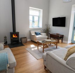 A living room with two beige sofas a wicker chair a wood burning stove a wall mounted tv and a blue door at Stapleford Farm in Hooke near Beaminster