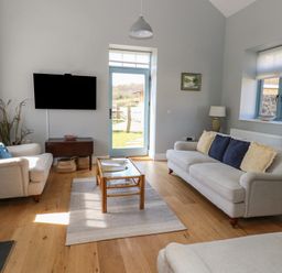 A living room with two sofas a coffee table a wall-mounted tv and a door leading outside at Stapleford Farm Hooke near Beaminster