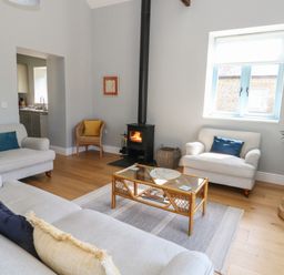 A living room with sofas a wicker chair coffee table and wood burning stove at Stapleford Farm in Hooke near Beaminster