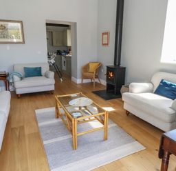 A living room with sofas a glass coffee table a wood-burning stove and a wicker chair at Stapleford Farm in Hooke near Beaminster