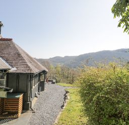 A gravel path beside a house with a slate roof and a green bush with hills in the background at Bwthyn y Coediwr in Tan Y Bwlch Maentwrog
