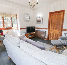 A living room with a gray sofa a gray armchair a television and wooden door at Bwthyn y Coediwr The Woodcutters Cottage in Tan Y Bwlch Maentwrog