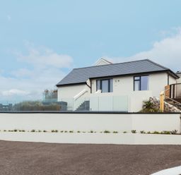 A modern white house with a slate roof glass balcony and outdoor seating at Shearwater in Mullion