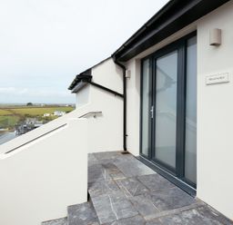 Stone steps leading to a glass door with a railing and a view of fields at Shearwater in Mullion