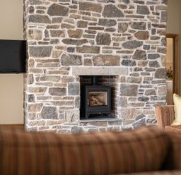 A living room featuring a stone wall and a wood burning stove at Trevean in Mullion