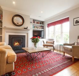 A living room with a fireplace two armchairs a sofa a coffee table with flowers and built in bookshelves at Sea Crest in Aldeburgh