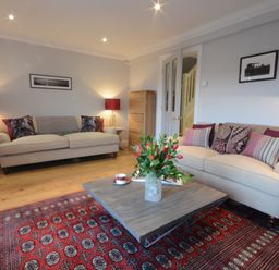 A living room with two beige sofas a wooden coffee table with flowers and a red patterned rug at Sea Crest Aldeburgh