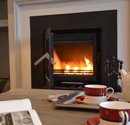 A fireplace with fire burning and a coffee table holding a white teapot and two red and white cups at Sea Crest in Aldeburgh
