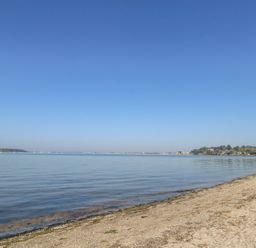 A sandy beach with calm water and a distant shoreline under a clear blue sky at Flat 7 Sand Acres in Canford Cliffs