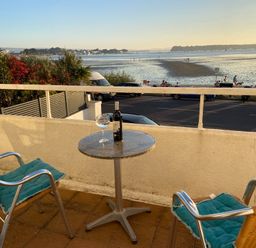 A balcony with two chairs and a small round table overlooking a beach with people and vehicles at Flat 7 Sand Acres in Canford Cliffs
