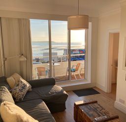A living room with a gray sofa pillows wooden chest and television near a balcony overlooking the sea at Flat 7 Sand Acres in Canford Cliffs