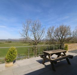An outdoor area with a wooden table and benches overlooking fields at Tirionfa in Talsarnau