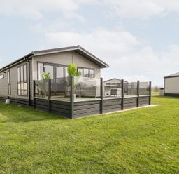 A modern single story house with a glass fenced deck and outdoor furniture on a grassy lawn at Summerdown in Brean