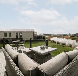 A deck with wicker sofas and a table overlooking a pond and multiple lodges at Summerdown in Brean