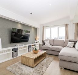 A living room with a large sectional sofa wooden coffee table wall-mounted television and shelves at Summerdown Brean