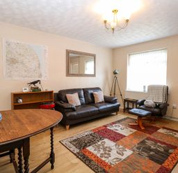 A living room with a brown leather sofa two chairs a wooden table a colorful rug and a tripod lamp at Sweetacres in Hemsby