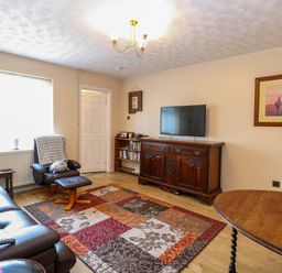 A living room with leather sofa recliner chair wooden cabinet flat screen TV bookshelf and patterned rug at Sweetacres in Hemsby