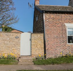 A stone wall with a white gate and daffodils in front of a brick house at Top Holme Cottage in Newbald
