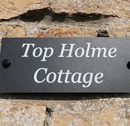 A black sign with white text reading Top Holme Cottage mounted on a stone wall at Top Holme Cottage in Newbald
