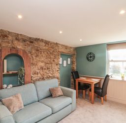 A sitting room with a blue sofa and wooden table with two chairs near a window at Top Holme Cottage in Newbald