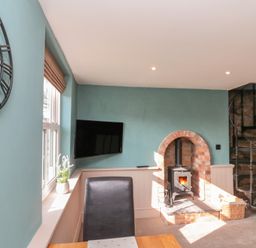 A room with a wall clock window with plant wall mounted television wood burning stove and spiral staircase at Top Holme Cottage in Newbald