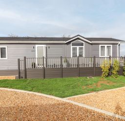 A single story grey house with white trim a front porch with railing and a gravel driveway at The Gallops in Chipping Norton