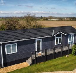 A single-story dark blue house with white windows and a black roof surrounded by fields at The Gallops in Chipping Norton