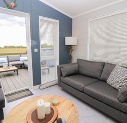 A living room with grey sofas a round wooden table with candles and a lamp near a window at The Gallops in Chipping Norton