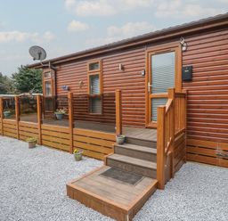 An exterior view of a wooden cabin with steps leading to a door surrounded by gravel and small potted plants at Lodge 2 in Auchterarder