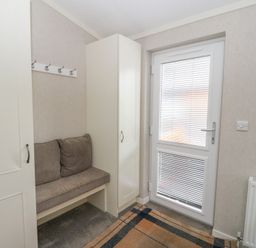 An entryway with a cushioned bench between two cabinets a wall-mounted coat rack and a door with blinds at Lodge 2 in Auchterarder