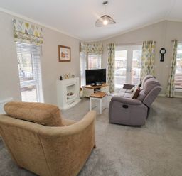 A living room with sofas a TV on a stand a small table a fireplace and windows with patterned curtains at Lodge 2 in Auchterarder