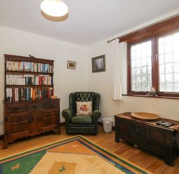 A room with a wooden bookshelf filled with books an armchair a wooden chest under a window and a patterned rug on the floor at Wringford Farm Annexe Rame near Kingsand