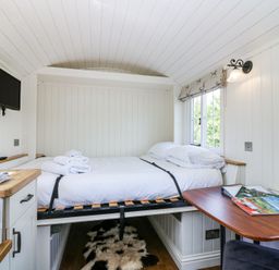 A small bedroom with a bed, a wall-mounted TV, a wooden table with magazines, and a window with a Roman blind at Airlie Burnside near Forfar