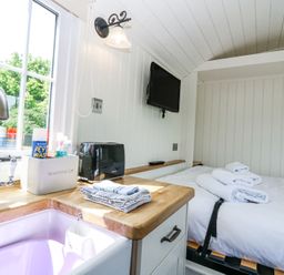 A small kitchen area with a sink toaster and cloths next to a bed with towels and a wall mounted tv at Airlie Burnside near Forfar