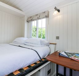 A small bedroom with a white bed and pillows next to a window with deer patterned blind and a wooden table with magazines at Airlie Burnside near Forfar