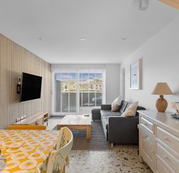 A living room with a sofa a coffee table a mounted TV and a dining table with chairs at 5 Mermaid Court in Newquay