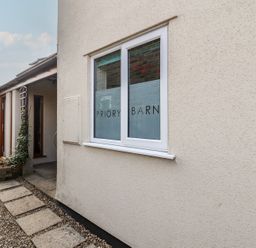 Exterior view of a building with a window displaying Priory Barn and a gravel path leading to a covered entrance at Priory Barn Apartment in Walton near Street