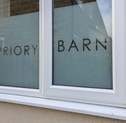 A close up of a window with frosted glass and the words PRIORY BARN on it
