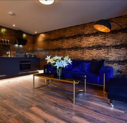 A living area with a blue sofa a gold and black coffee table with white flowers and a kitchen area at Wayside Lodge in Blackpool