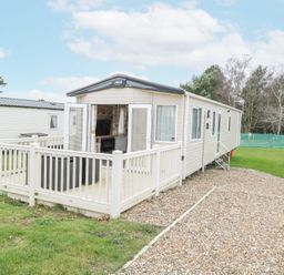 A static caravan with an open patio door and railing on a gravel driveway surrounded by grass at 75 Foxburrow Hang in Fritton