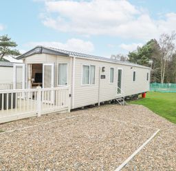 A mobile home with a small fenced deck and gravel driveway surrounded by grass and trees at 75 Foxburrow Hang in Fritton