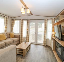 A living room with beige sofas a wooden coffee table TV and fireplace at 75 Foxburrow Hang in Fritton