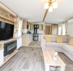 A living room with a sectional sofa and a coffee table next to a kitchen area at 75 Foxburrow Hang in Fritton