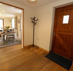 An entryway with a wooden front door and a coat rack next to an open dining room with a table and chairs at Little Dairy House near Swanage