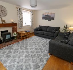 A living room with two dark sofas a fireplace a wooden coffee table and a gray rug at Little Dairy House near Swanage