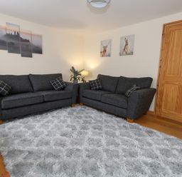 A room with two dark gray sofas a gray rug a wooden door and wall art at Little Dairy House near Swanage