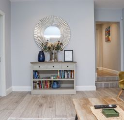 A room with a wooden floor a console table with books vases flowers and a round mirror above Daly's Place Ballyporeen County Tipperary