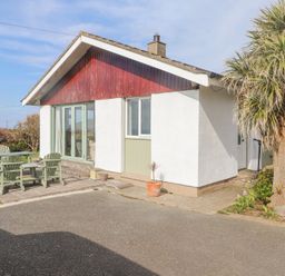 An exterior view of a single-story house with a small patio set and a tree at Seafield in Rhydwyn near Cemaes Bay