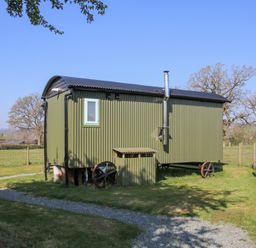 A green corrugated metal shepherds hut with black roof and wheels on a grass field at Gilberry Shepherds Hut in Wall under Heywood near Church Stretton