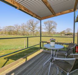 An outdoor seating area with two chairs a small table and a potted plant overlooking a grassy field at Gilberry Shepherds Hut in Wall under Heywood near Church Stretton